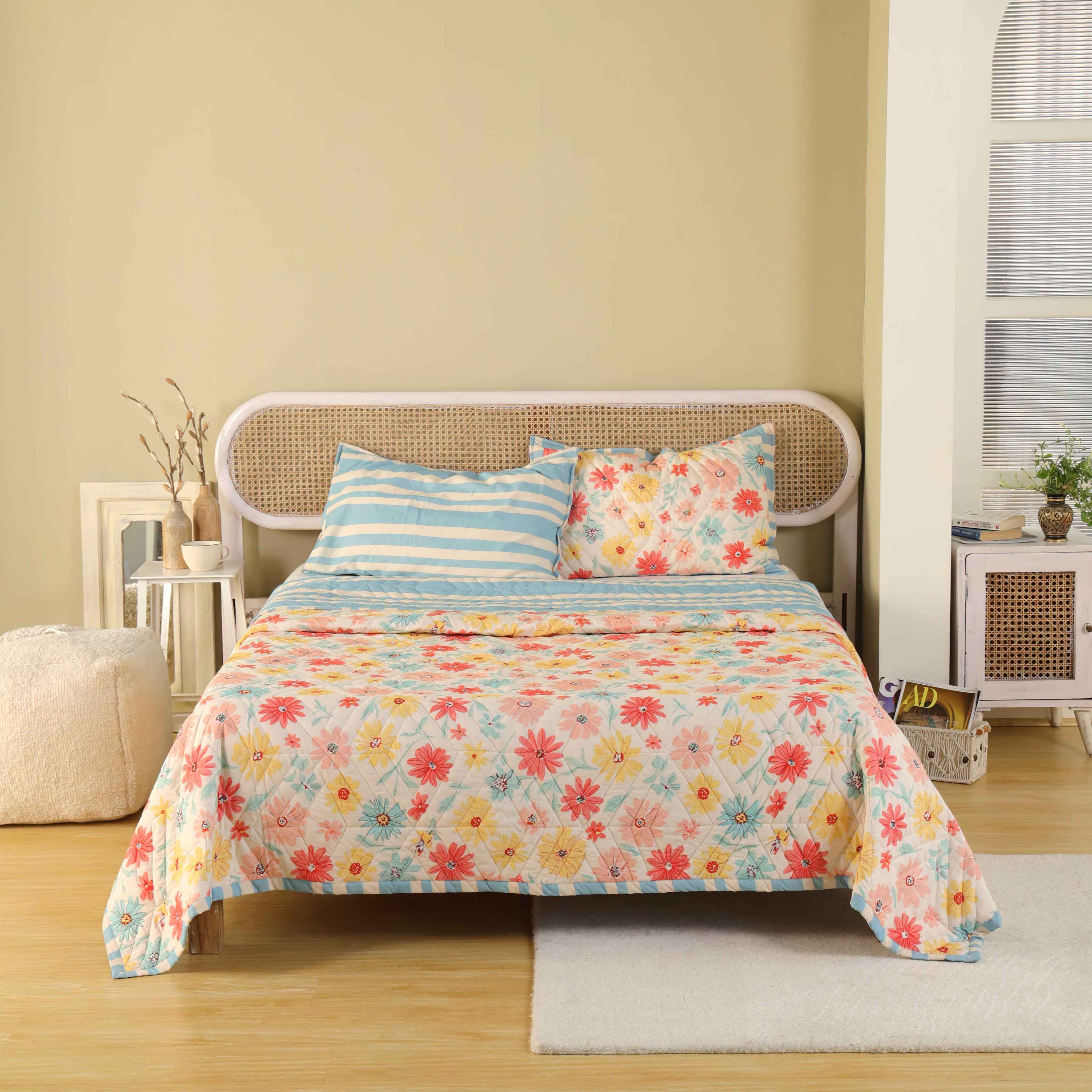 3-piece reversible cotton quilt set with wildflower print and blue striped reverse on a bed.