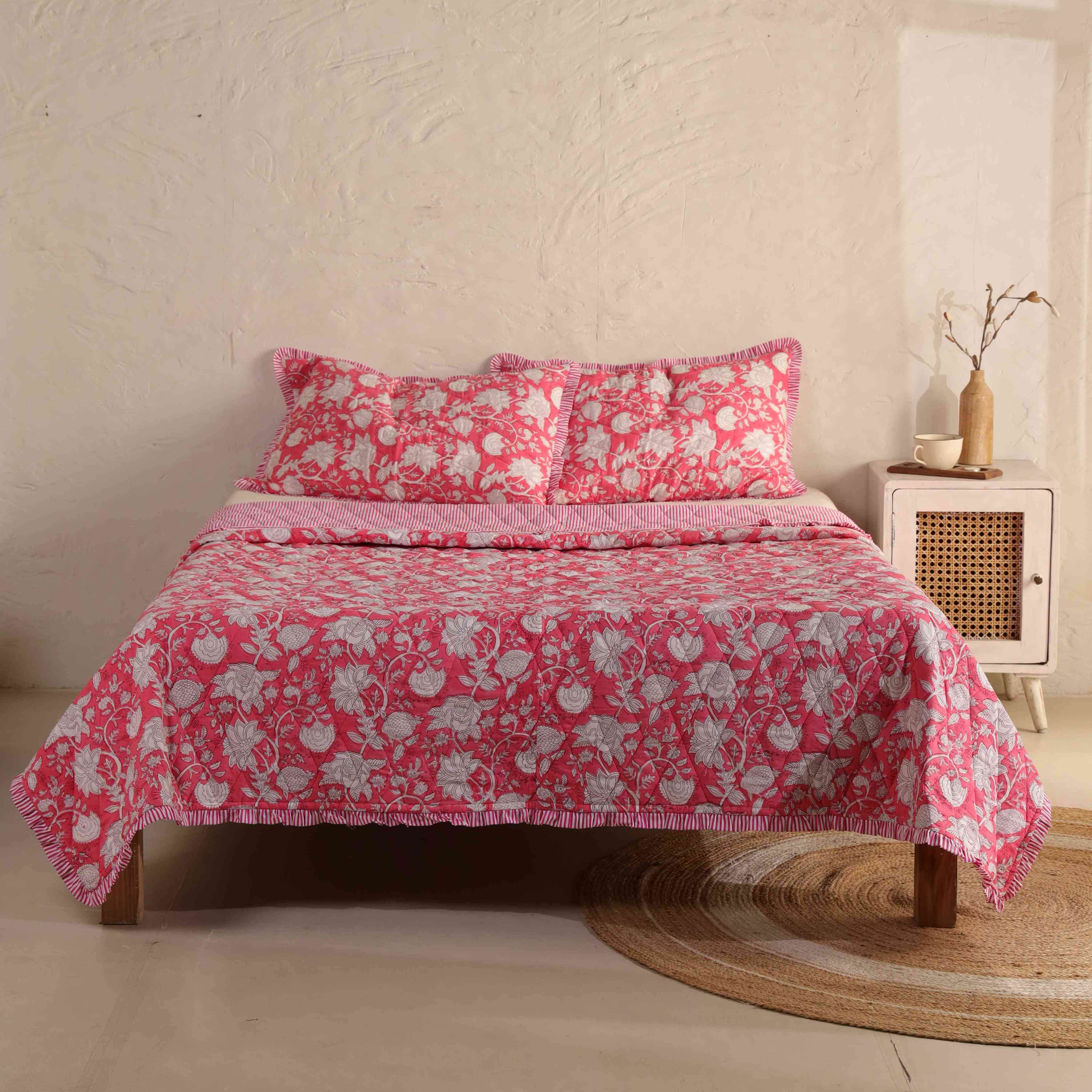 3-piece deep rose pink floral quilt set with striped ruffle edges on a bed.