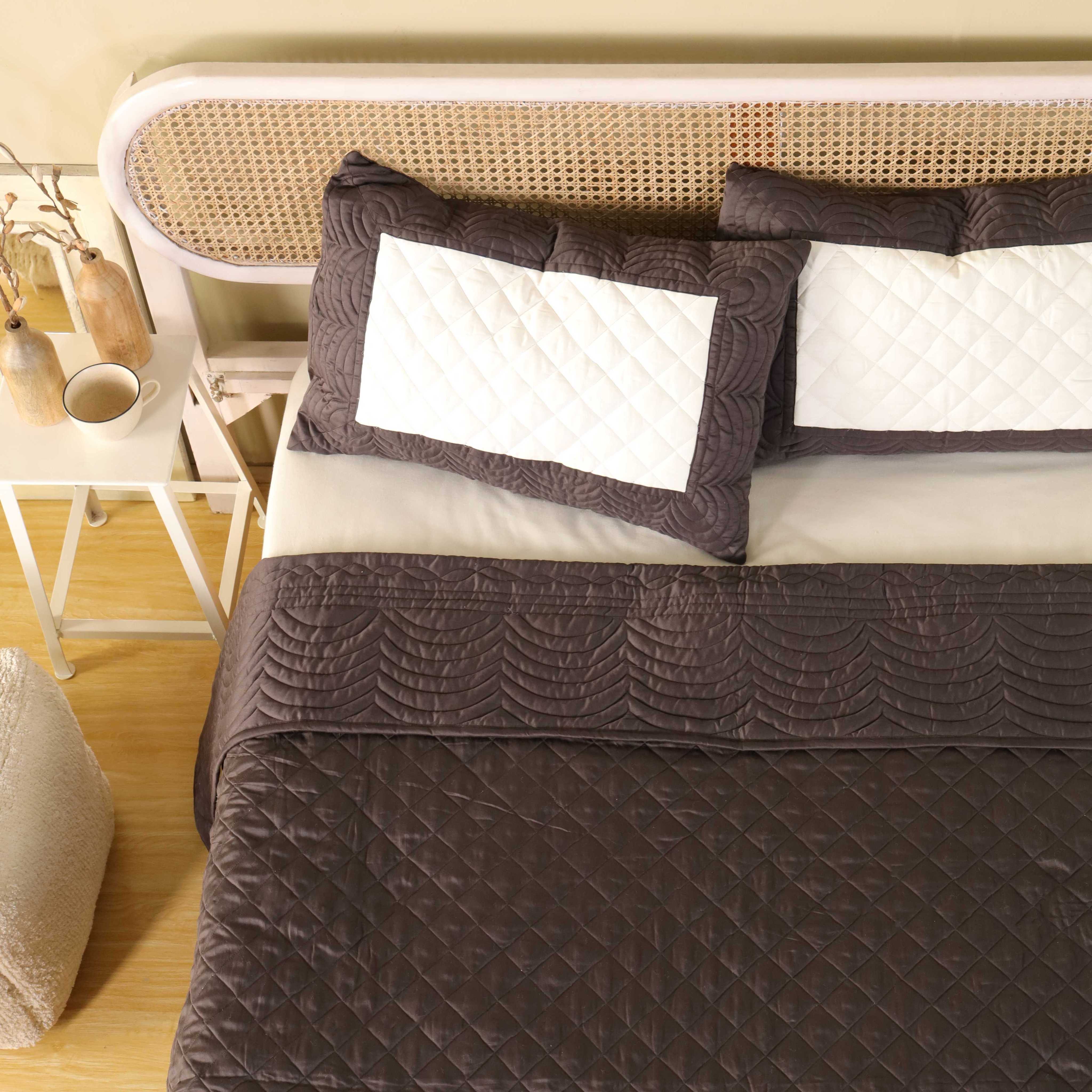The scalloped edge of the chocolate brown satin quilt draped over a bed.