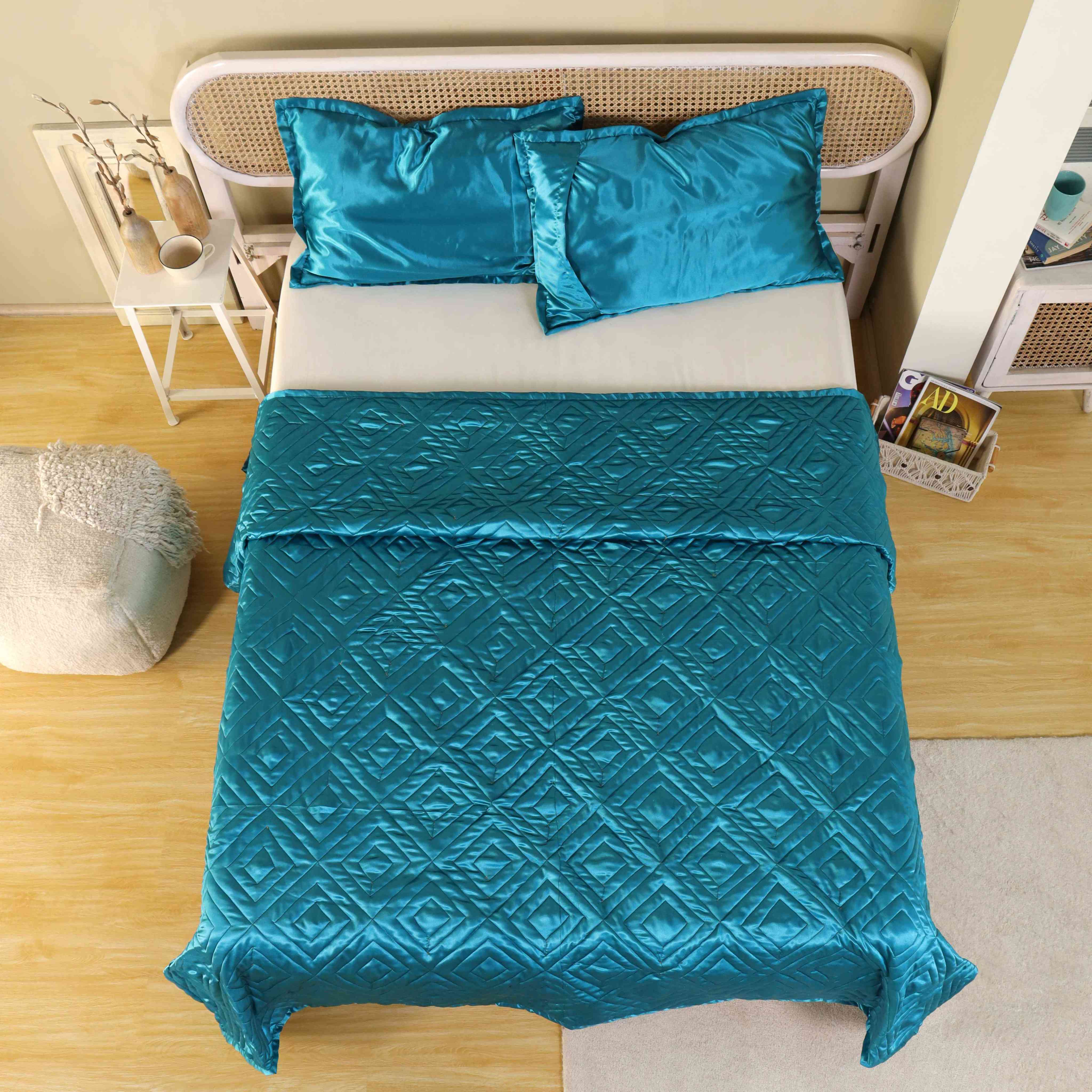 Luminous teal blue satin duvet cover with intricate diamond quilting on a modern bed.