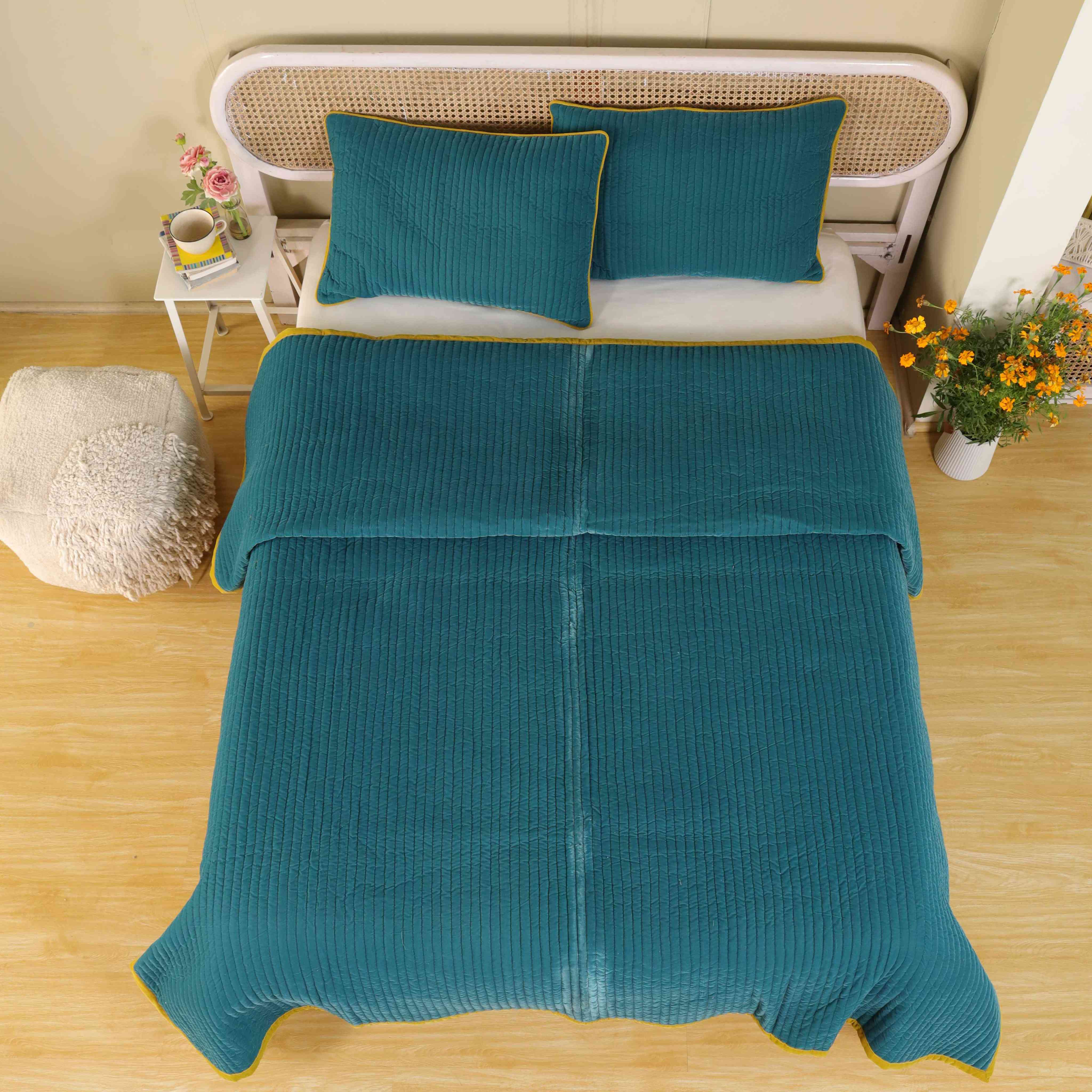 Teal blue velvet duvet cover with mustard yellow trim and vertical quilting on a bed with a cane headboard.