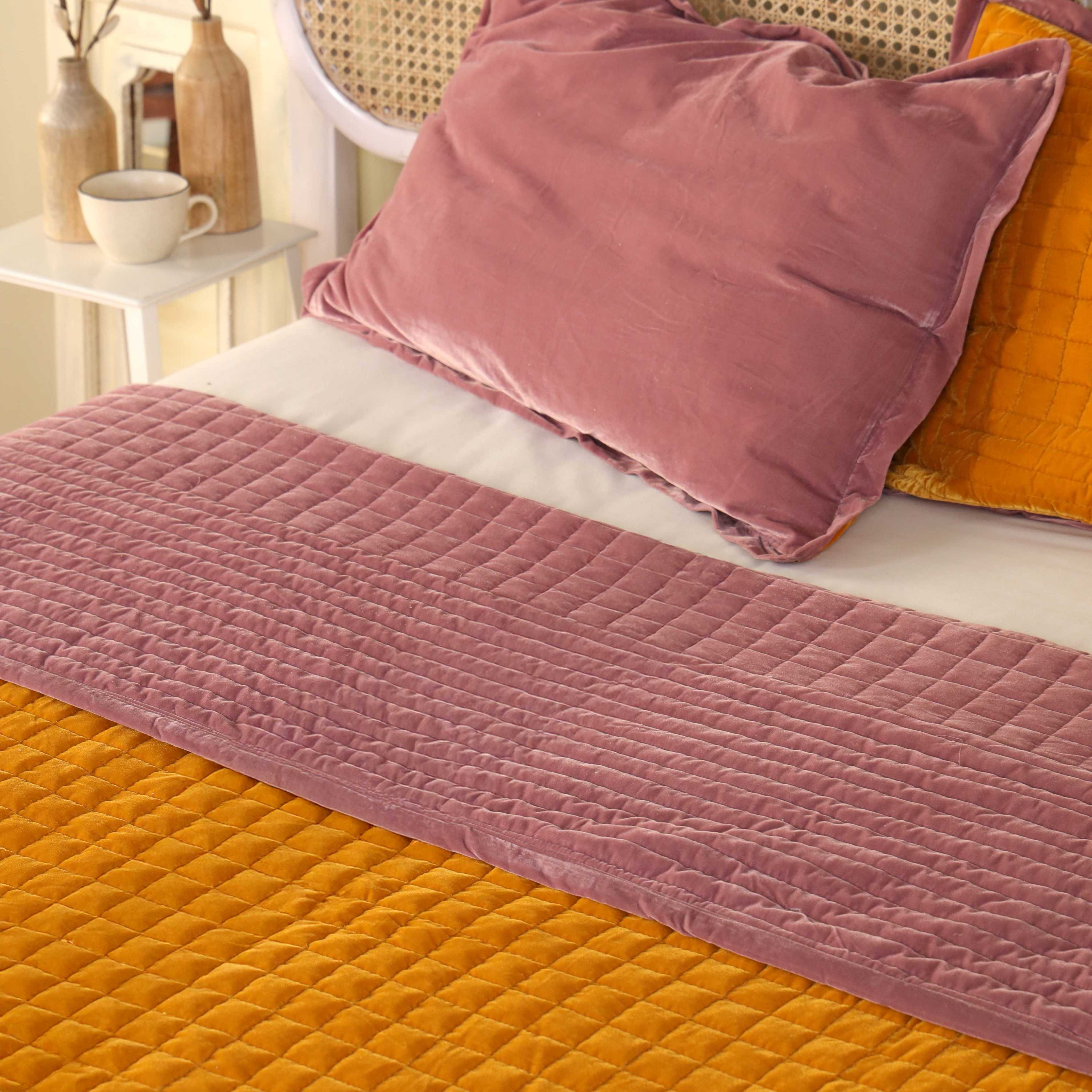 Matching mustard yellow and dusty pink quilted velvet pillow covers resting on a modern bed.